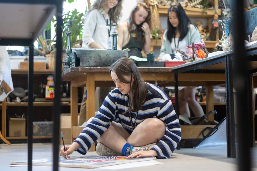 Student sitting with legs crossed and arm extended, painting on canvas in Art and Design A Level at St David’s Catholic Sixth Form College in Cardiff