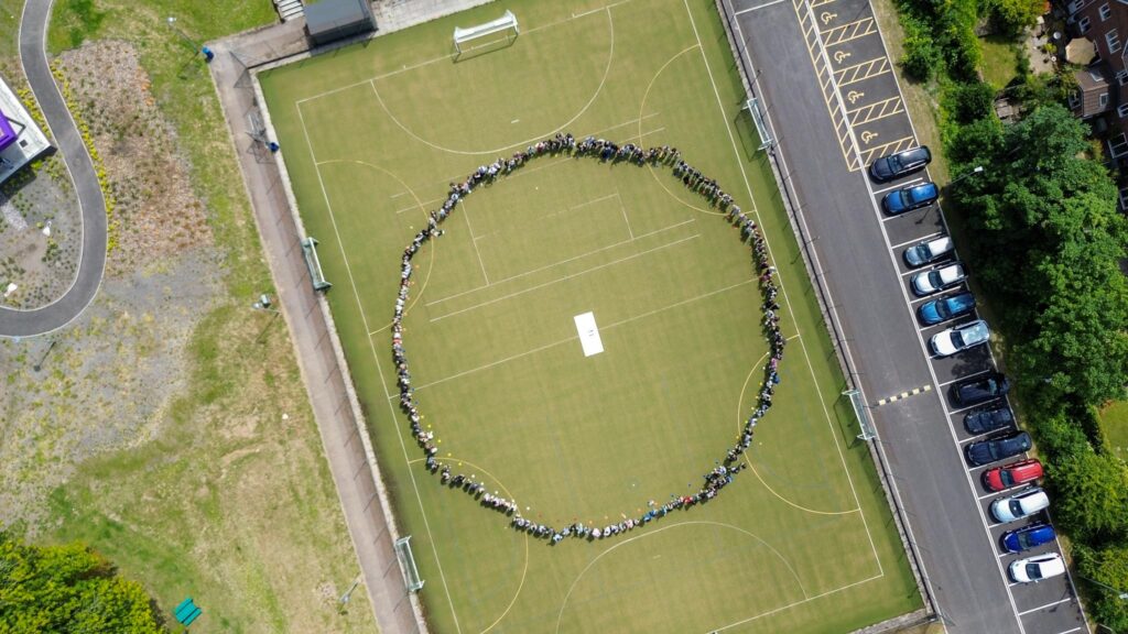 A drone shot of students and staff holding hands in a circle for 'World Refugee Week'