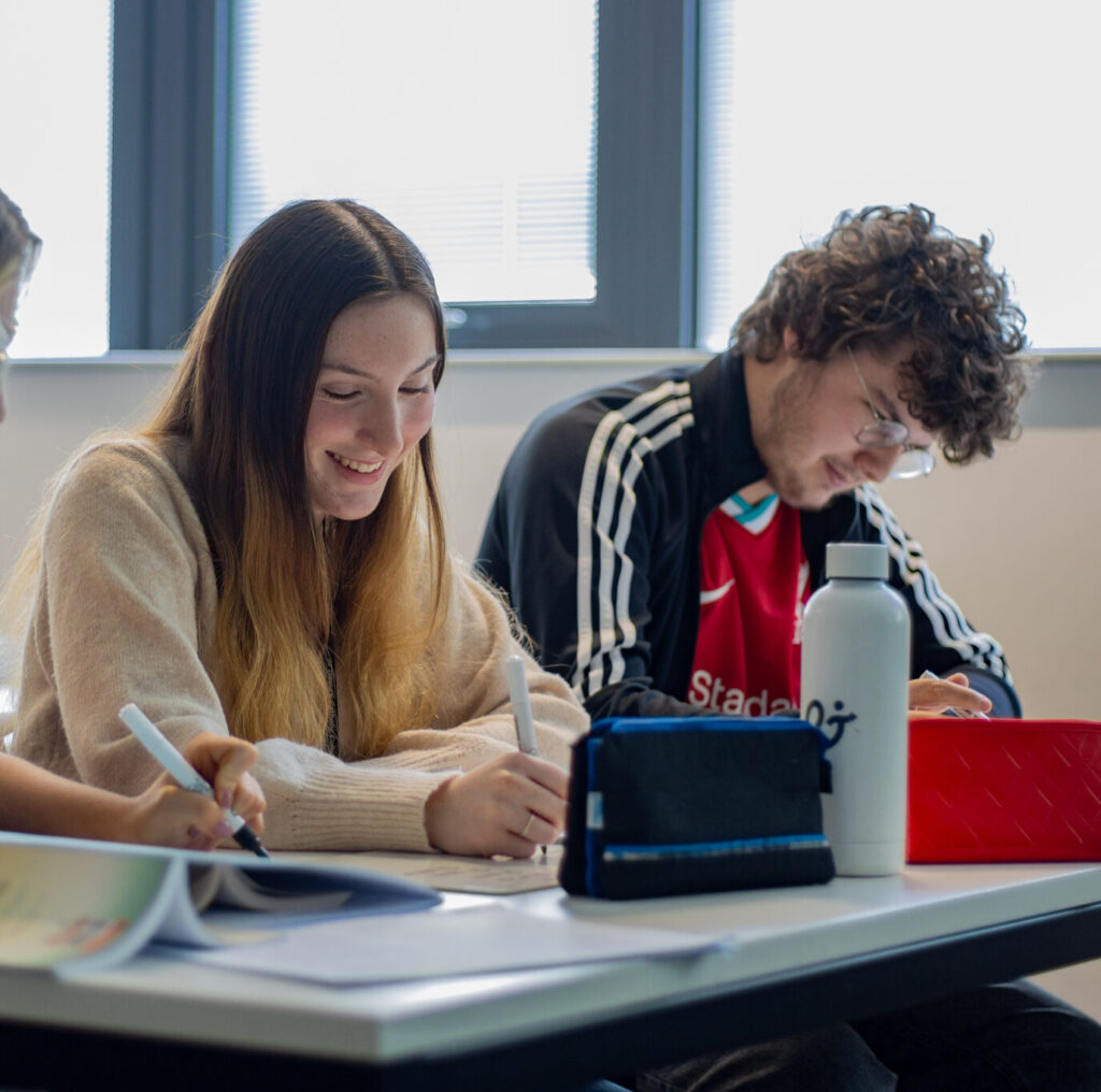 A Level French lesson in St David's Catholic Sixth Form College with a student smiling with others whilst scribbling down notes