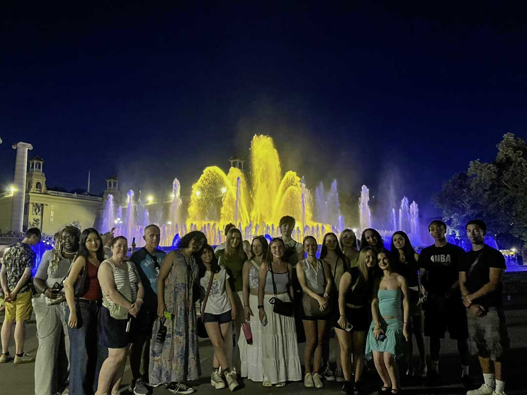 Students in front of a lit up fountain at night